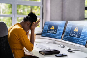 stressed hacked computer hands on head crying desk hacker head down