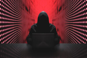 Anonymous hacker in front of his computer with red light wall backgroundAnonymous hacker in a black hoody with laptop in front of a code background with binary streams cyber security concept brute force